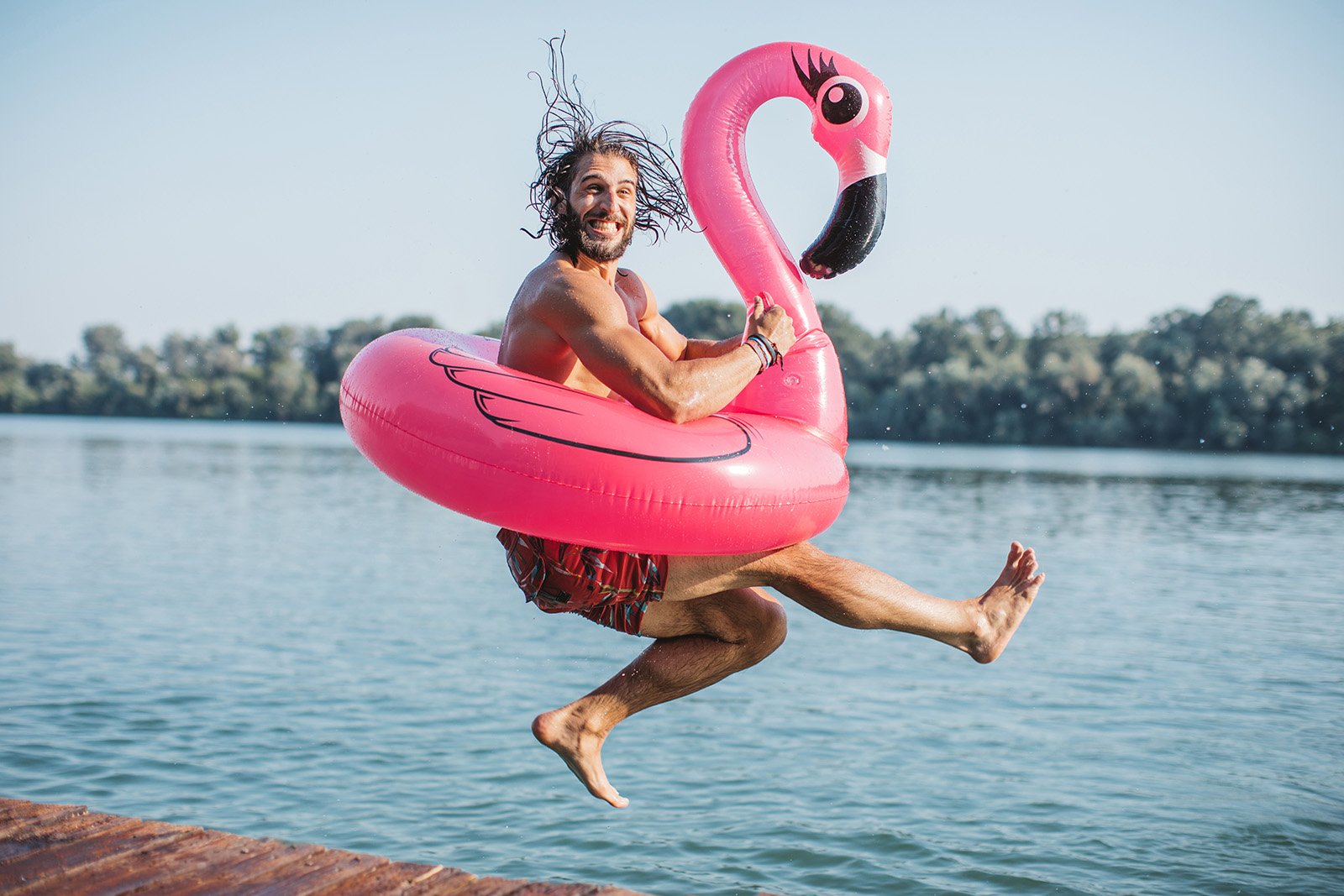 Mann hopper i sjøen med badeflamingo og er glad Mann hopper i sjøen med badeflamingo og er glad